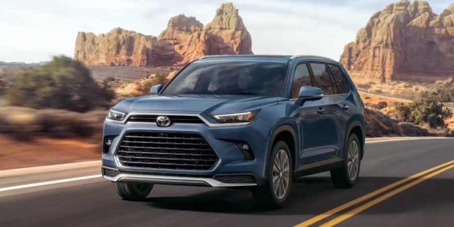 A blue 2024 Toyota Grand Highlander three-row midsize SUV is driving on the road.