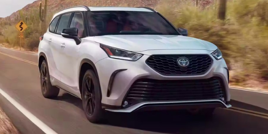 A white 2023 Toyota Highlander midsize SUV is driving on the road.