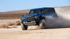 A blue 2022 Ford Bronco Raptor undergoing off-road driving training through dirt and sand