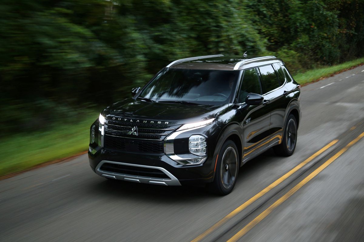 A black 2023 Mitsubishi Outlander PHEV plug-in hybrid compact SUV model driving on a forest highway