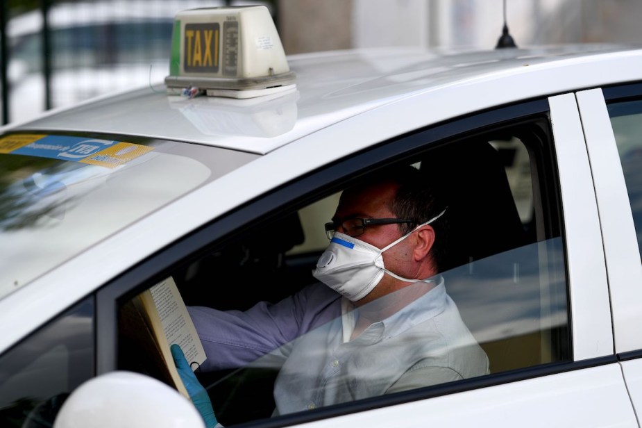 A taxi driver reads a book as he waits in his taxicab.