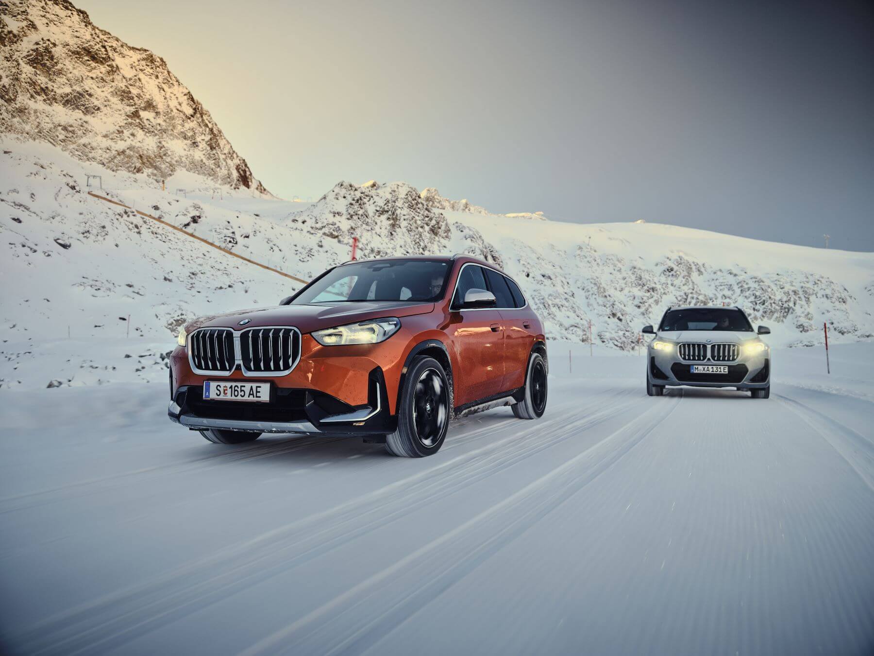 Orange and gray BMW X1 xDrive23d and XDrive30 models driving through the snow near mountains