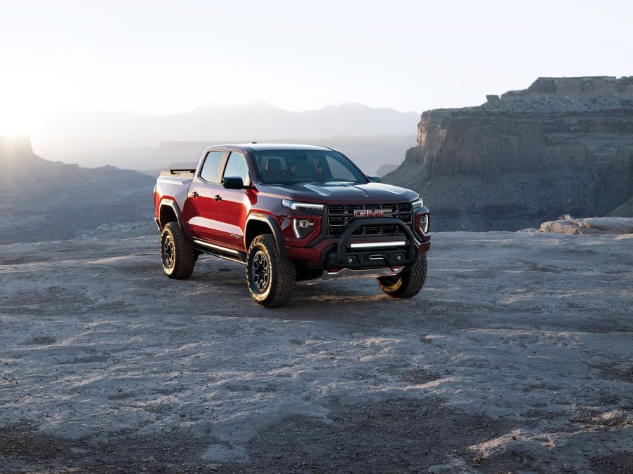 A red 2023 GMC Canyon AT4X Edition 1 midsize pickup truck model on top of a rocky cliff in the wilderness