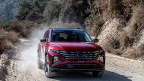 A red 2023 Hyundai Tucson compact SUV model driving on a dirt road as its tires kick up dust