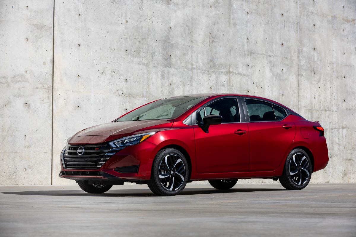 A red 2023 Nissan Versa subcompact sedan model parked in front of a concrete wall