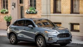 A steel blue 2023 Honda HR-V EX-L subcompact crossover SUV model parked in front of a yellow brick buildiing