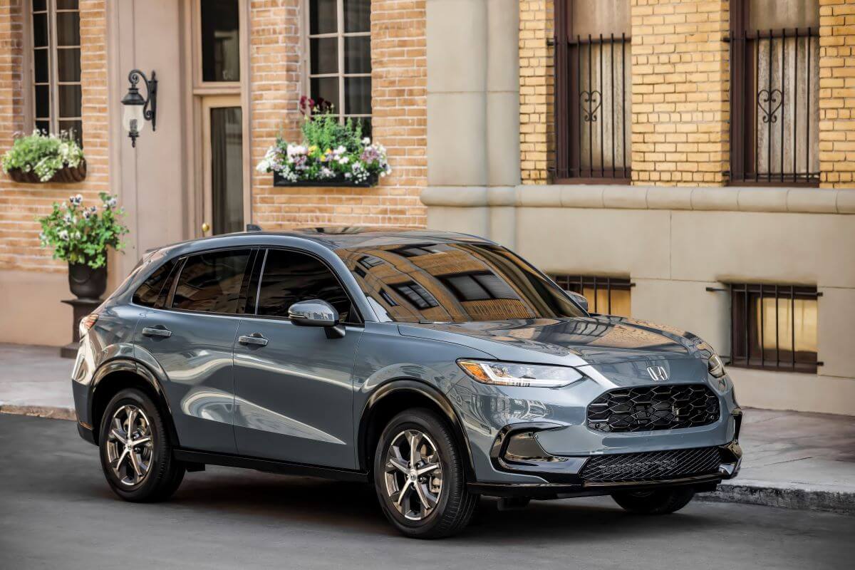 A steel blue 2023 Honda HR-V EX-L subcompact crossover SUV model parked in front of a yellow brick buildiing