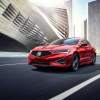 A red Acura ILX driving down a road within a city.