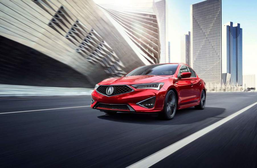 A red Acura ILX driving down a road within a city.