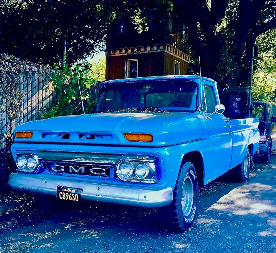 A blue GMC classic pickup truck parked on the street in California, trees visible in the background.