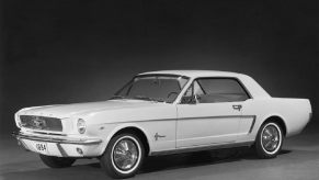 A first-generation 1965 Ford Mustang, what fans call the 1964 1/2 model, shows off its white paintwork and Ford Falcon platform on a stage.