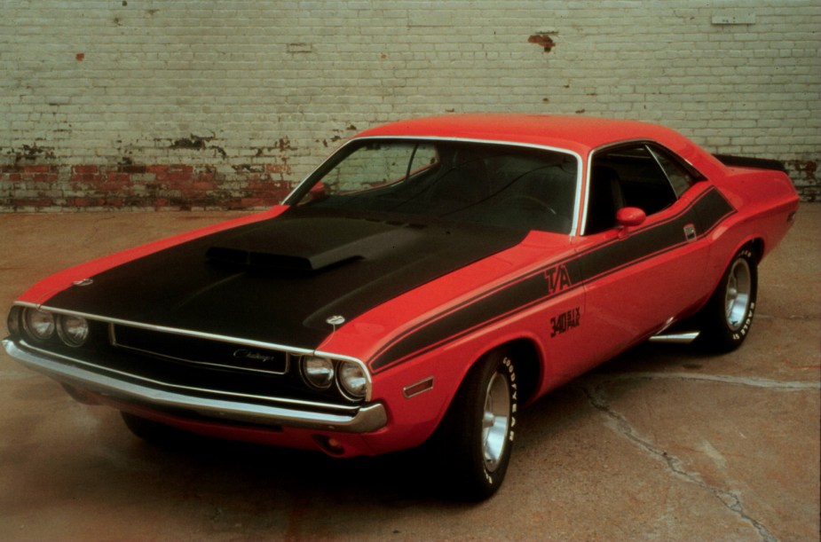 A red 1970 Dodge Challenger T/A collectible classic muscle car parked in front of a white brick wall.