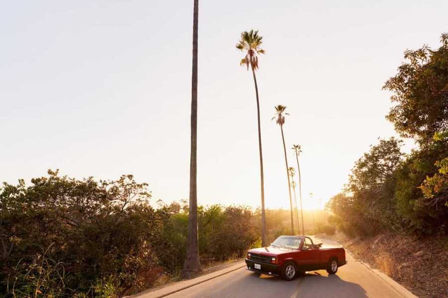 A Dodge Dakota sport convertible pickup truck parked in front of a row of palm trees on a California road for a photo.