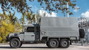 Promo photo of a Land Rover Defender 6x6 truck up for auction, a power station visible in the background.