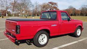 Red Ford F-150 Lightning used supertruck in a parking lot, trees visible in the background.