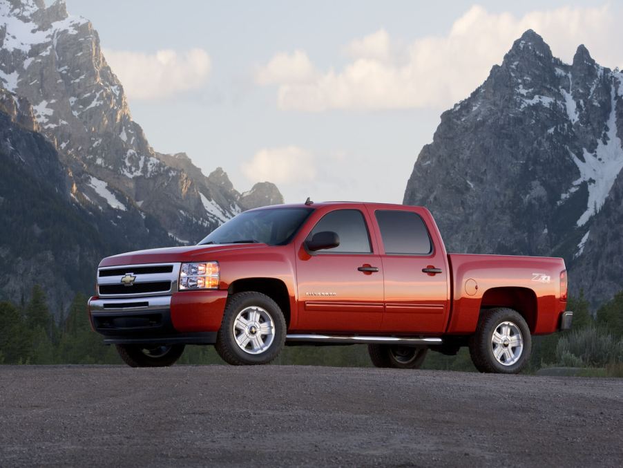 Promo photo of a red 2011 Chevrolet Silverado 1500 pickup truck parked in front of snow-capped mountains.