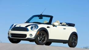 A white and black 2011 Mini Cooper Convertible model parked at the top of an asphalt hill road