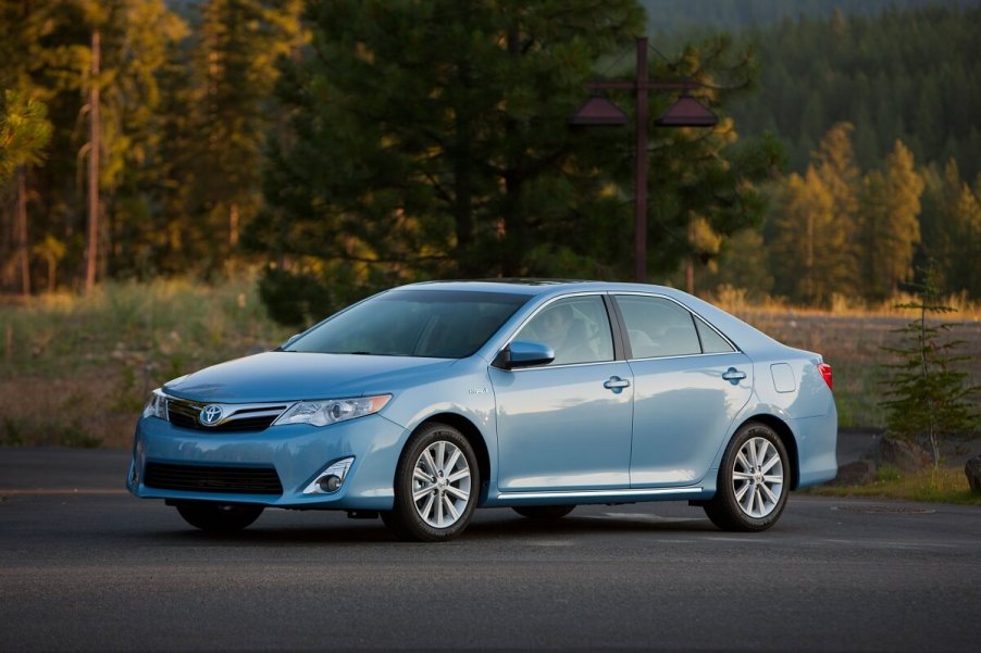 A used 2012 Toyota Camry Hybrid in blue cruises country roads.