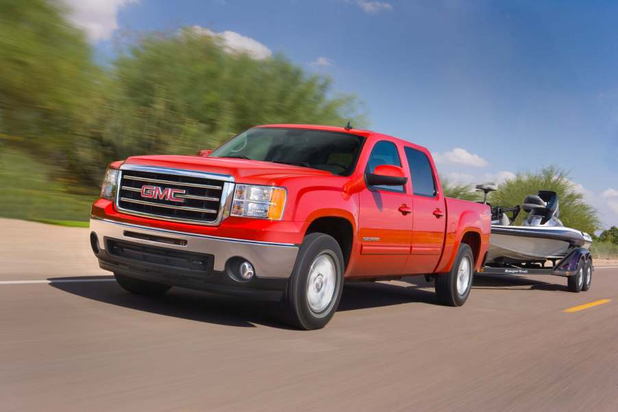 Red 2013 GMC Sierra 1500, a truck with relatively few engine issues, towing a boat down a rural road with trees in the background.