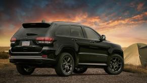 A black 2020 Jeep Grand Cherokee in front of a sunset with a tent in the background.