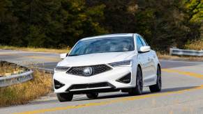 A white 2021 Acura ILX driving down a curvy road in a woody area.