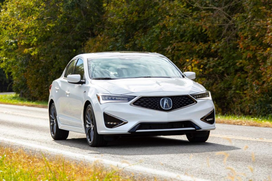 A white 2021 Acura ILX driving down a wooded country road. 