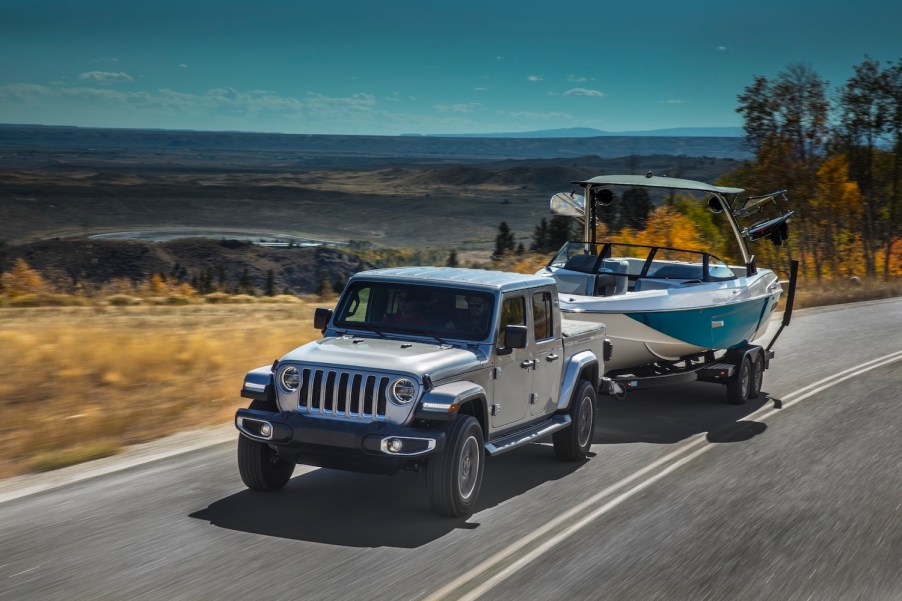 A silver 2021 Jeep Gladiator pickup truck tows a boat up a mountain road to show its Ram 1500 levels of capability.