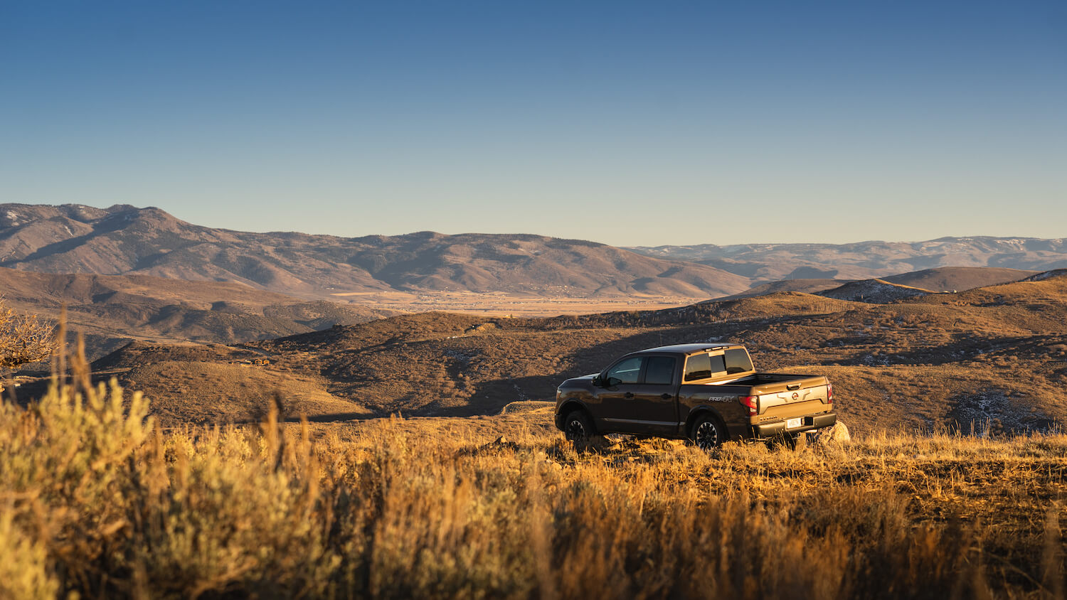 A V8 Nissan Titan crew cab parked off-road in a field, with a ridgeline of mountains visible in the distance to demonstrate its 4WD.