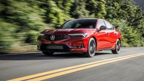 A red 2023 Acura Integra sports car shows off its liftback while it cruises down a safe back road.