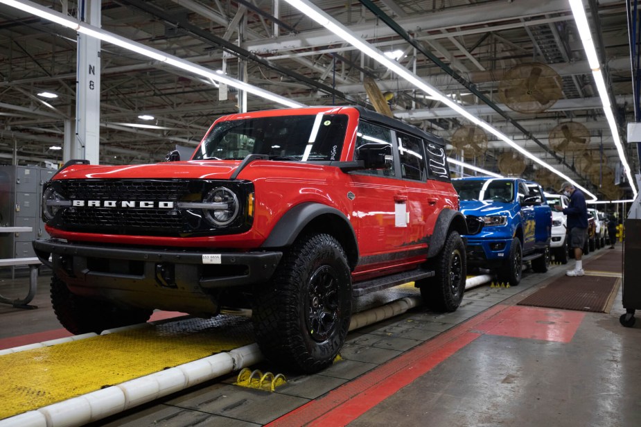 Red Ford Bronco rolls down an assembly line ahead of a blue Ford Ranger.