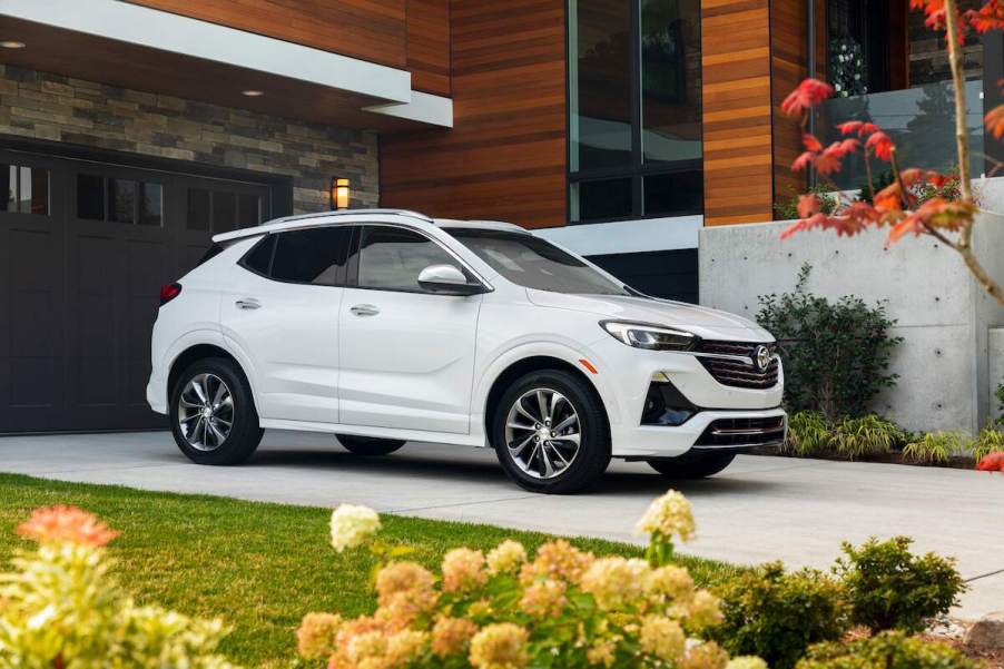 A white 2023 Buick Encore GX parked in a driveway of a brown and white building.