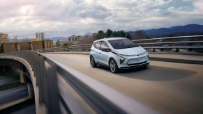 A light blue 2023 Chevrolet Chevy Bolt EV model driving on a highway overpass