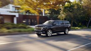 A black 2023 Chevy Suburban High Country full-size SUV model driving on a suburban neighborhood street