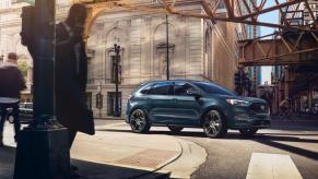 A blue 2023 Ford Edge midsize SUV model driving through a city crosswalk under metal girders