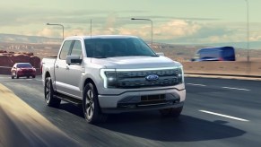 A white 2023 Ford F-150 Lightning electric pickup truck is driving on the road.