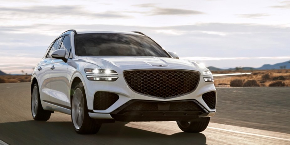 A white 2023 Genesis GV70 small luxury SUV is driving on the road. 