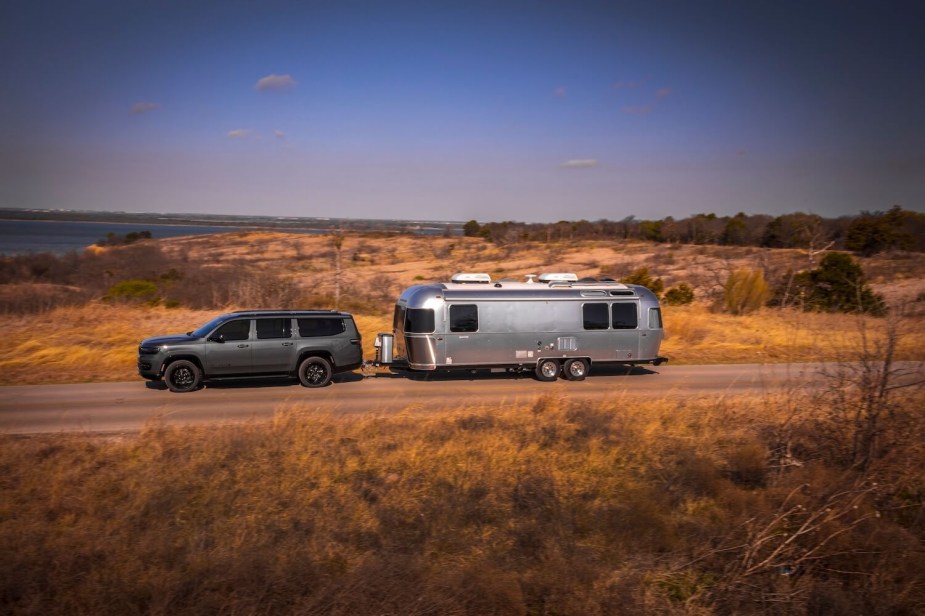 Promo photo of a gray Grand Wagoneer Jeep SUV towing a trailer with its independent rear suspension.