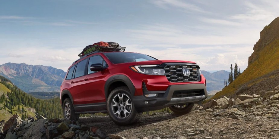 A red 2023 Honda Passport midsize SUV is parked off-road on a hill. 