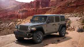 A 2023 Jeep Wrangler Rubicon scales red rocks in the desert. It's rated as one of the most reliable American SUVs of 2023.