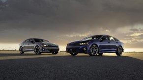 A pair of 2023 Kia K5 GT-Line models pose under an overcast sky.