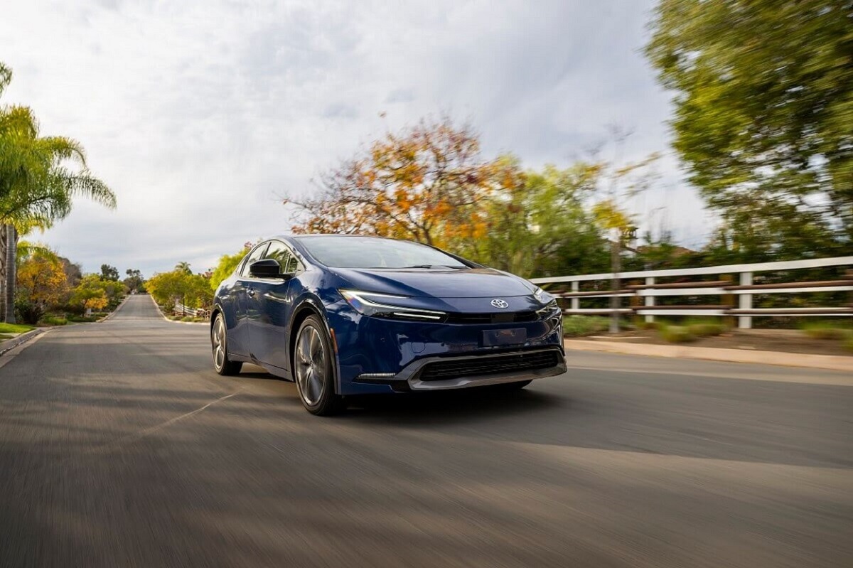 A blue Toyota Prius cruises the countryside on a one-car road.