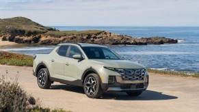 A beige 2023 Santa Cruz parked in front of the ocean and a rocky area in the sand.