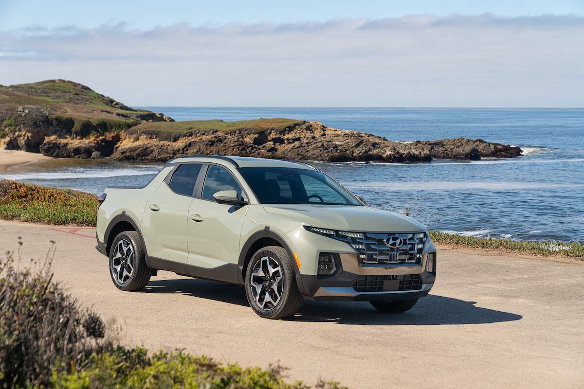 A beige 2023 Santa Cruz parked in front of the ocean and a rocky area in the sand.