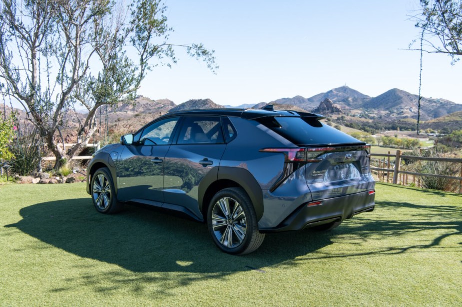 View from the rear of a 2023 Subaru Solterra EV sitting on green grass with mountains in the background. 