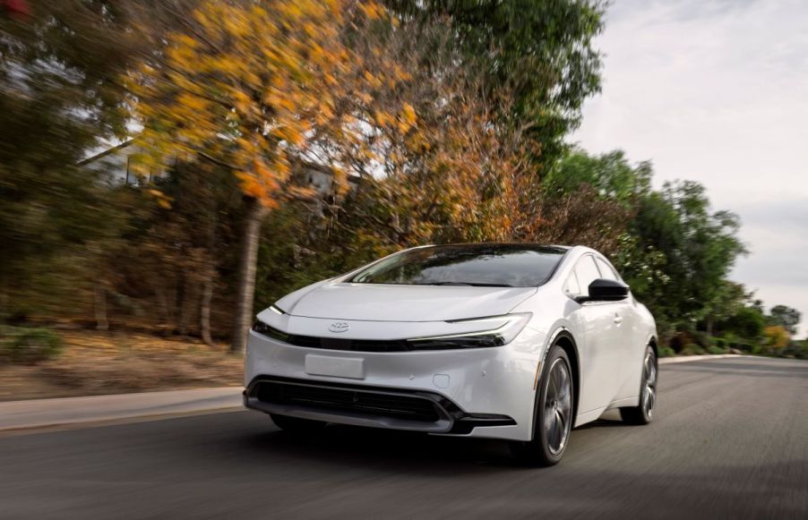 The all-new 2023 Toyota Prius drives down a road near some trees