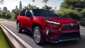 A red 2023 Toyota RAV4 Prime small plug-in hybrid SUV is driving on the road.