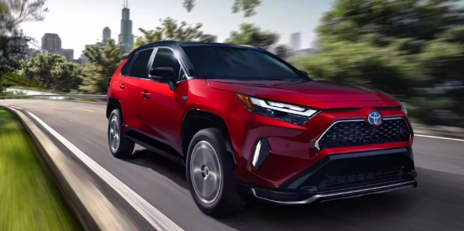 A red 2023 Toyota RAV4 Prime small plug-in hybrid SUV is driving on the road. 