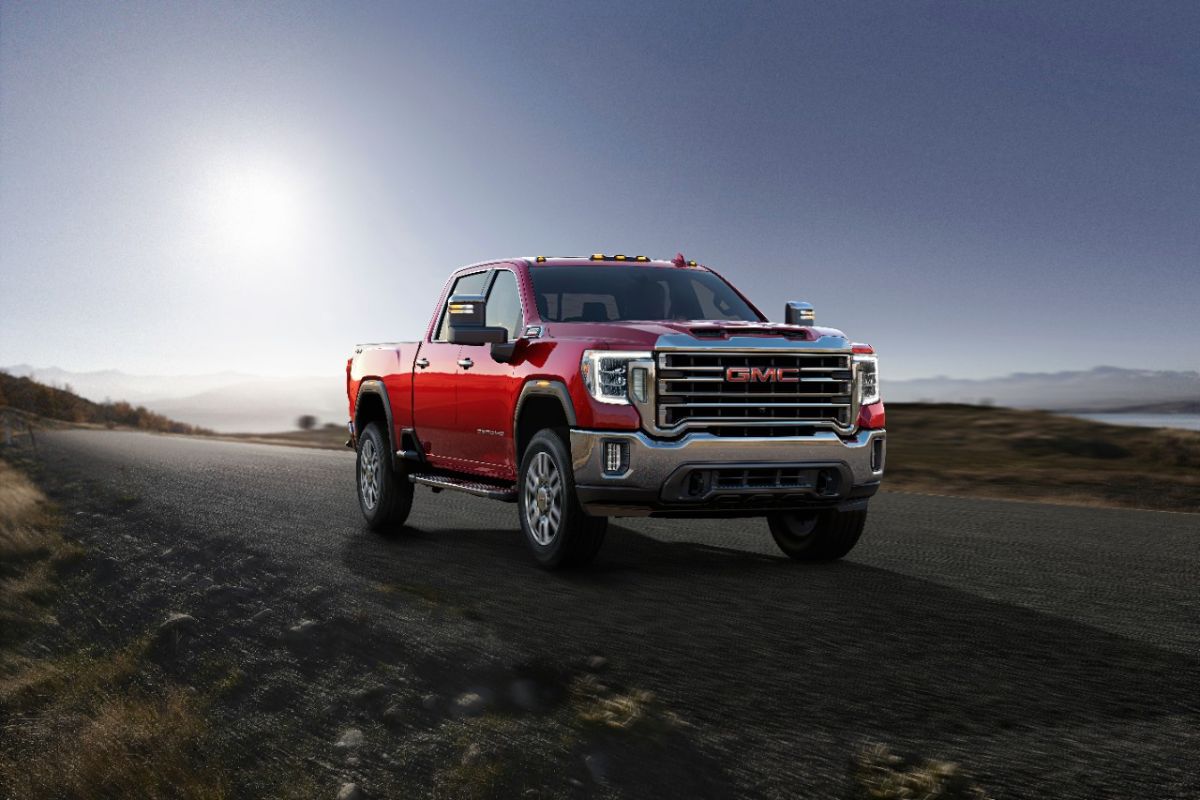 A red 2023 GMC Sierra 2500HD driving down a gravel road.