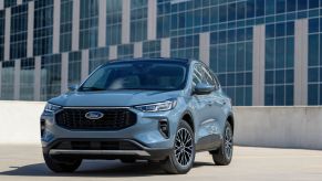 A light blue 2023 Ford Escape PHEV sits in front of a corporate building in bright daylight.