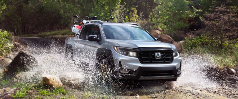 A new 2023 Honda Ridgeline pickup in silver drives through water.